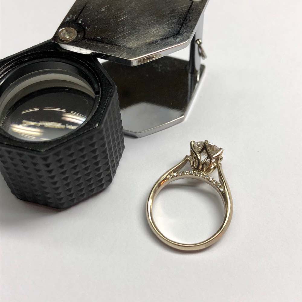 beautiful solitaire diamond ring lay flat with jeweler's loupe beside
